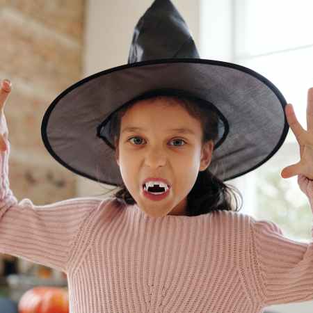 girl with vampire fangs and a witch hat